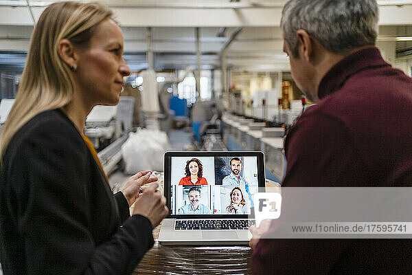 Businessman and businesswoman attending video call through laptop in factory