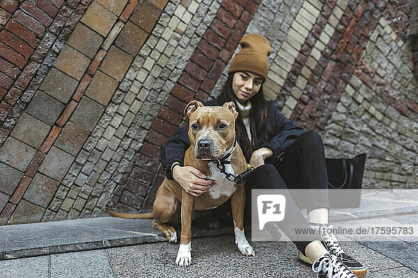 Young woman with dog sitting in front of wall