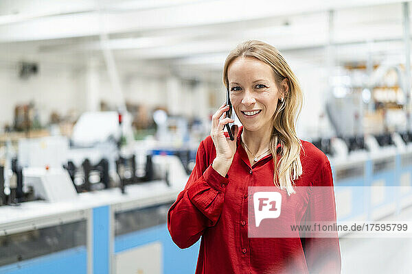 Smiling blond businesswoman talking on smart phone in factory