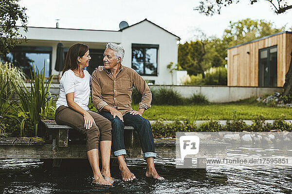 Lächelnde Frau und Mann schauen einander an  sitzend am See im Hinterhof