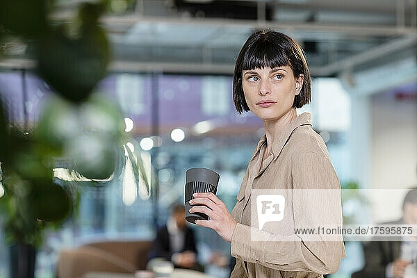 Thoughtful employee with disposable coffee cup in office lobby
