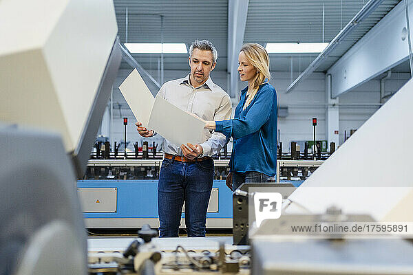 Blond businesswoman discussing over report with businessman in factory