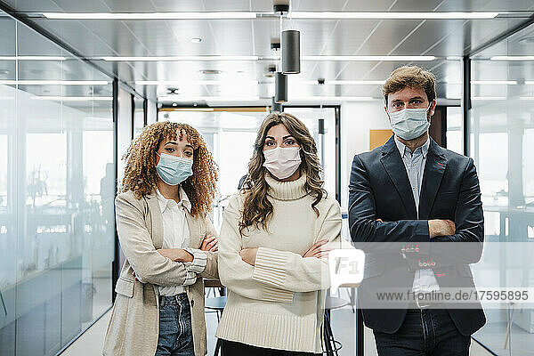 Businessman and businesswomen wearing protective face mask standing with arms crossed in office