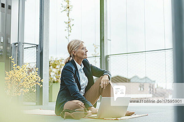 Nachdenkliche Geschäftsfrau mit Laptop sitzt im Büro