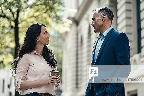 Businessman talking with businesswoman holding disposable coffee cup outside building