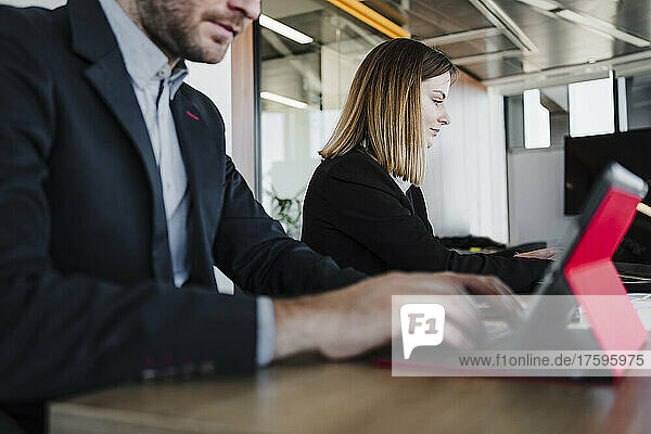 Young businesswoman sitting by colleague using tablet PC at desk in office