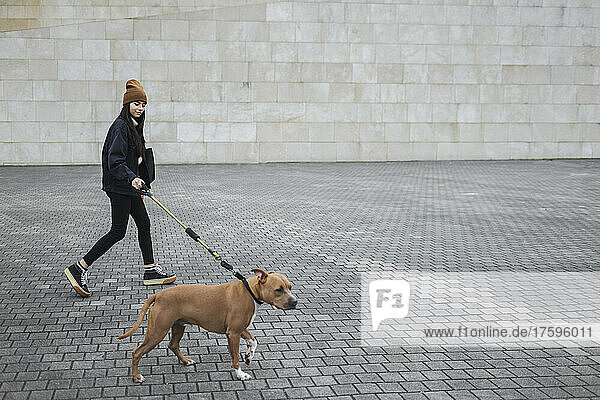 Woman with dog walking on footpath by wall