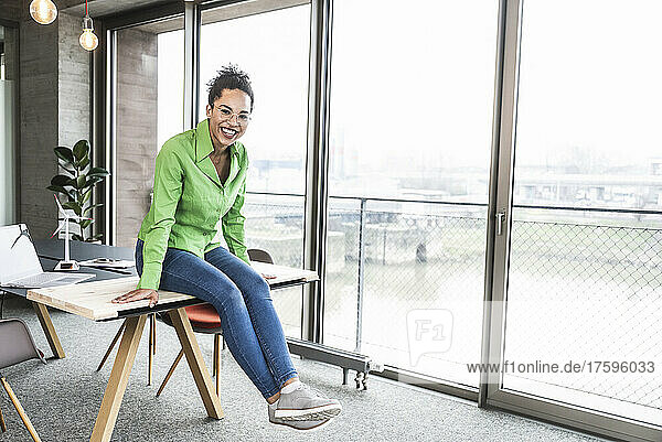 Happy businesswoman sitting on desk in office