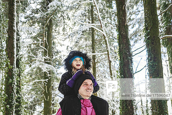 Happy man carrying daughter on shoulders in forest