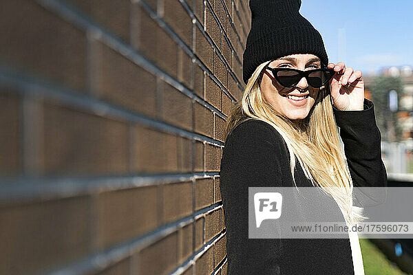Blond woman with sunglasses by brick wall