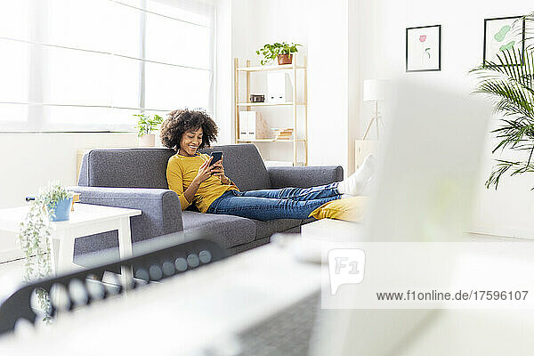 Smiling woman surfing net through mobile phone in living room