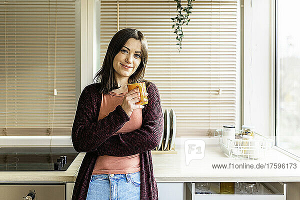 Smiling young woman holding mug in kitchen at home