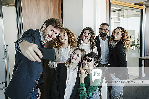 Happy businessmen and businesswomen taking selfie through mobile phone in office