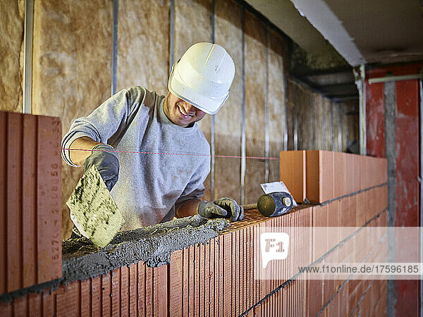 Smiling bricklayer applying cement on bricks working at construction site