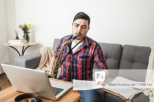 Man playing saxophone looking at music notes in living room at home