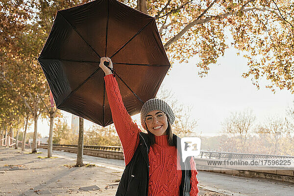 Smiling young woman holding umbrella standing on footpath