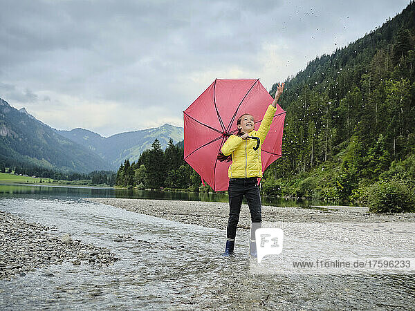 Mädchen mit Regenschirm spritzt Wasser am Seeufer