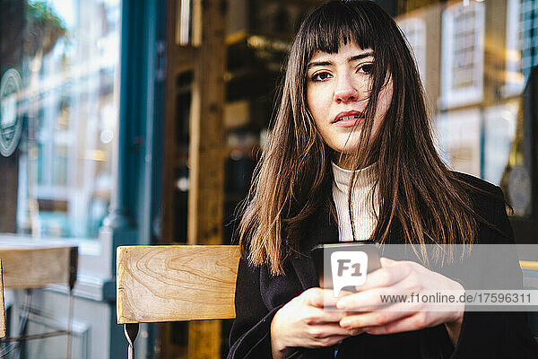 Schöne junge Frau mit Pony hält Smartphone im Straßencafé in der Hand