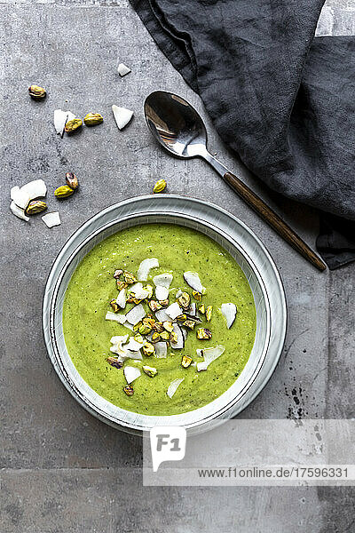 Studio shot of bowl of vegan pea soup with zucchini  broccoli  pistachios and coconut shreds