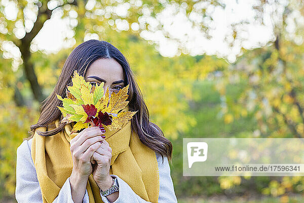 Junge Frau hält sich im Park Herbstblätter vors Gesicht