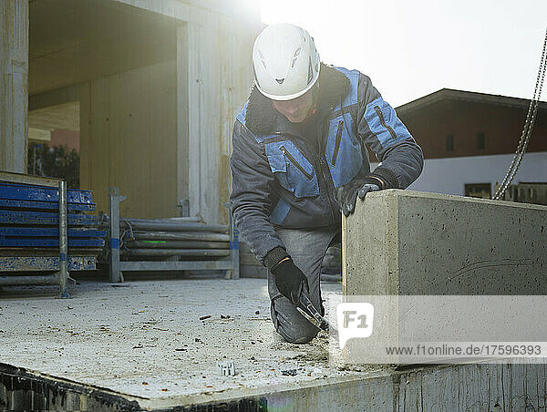 Worker cleaning corner of cement slab with hammer kneeling at construction site