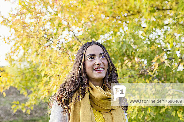 Happy young woman with yellow scarf in autumn park