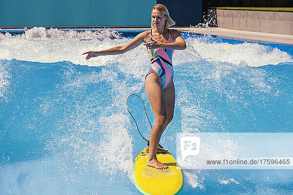 Young woman balancing on surfboard in swimming pool