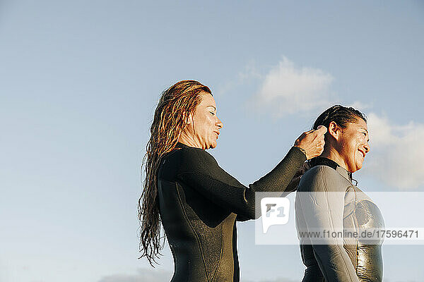 Smiling woman assisting surfer putting on wetsuit at beach