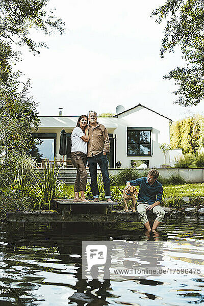 Mann und Frau stehen neben Sohn und Hund sitzen am See im Hinterhof