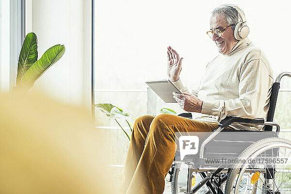 Smiling disabled man waving hand on video call through tablet PC at home