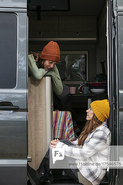 Two women wearing knit hats looking at each other sitting in van