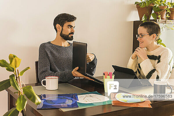 Businessman showing laptop to businesswoman at desk