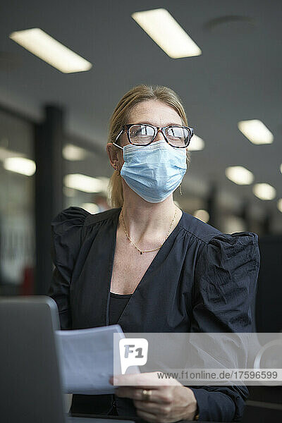 Businesswoman with document wearing protective face mask in office