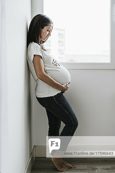 Pregnant woman leaning on wall at home