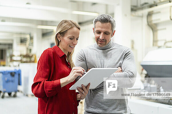 Smiling businesswoman sharing tablet PC with colleague in factory