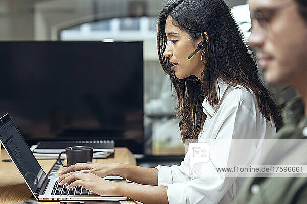 Junge Geschäftsfrau benutzt Laptop von Geschäftsmann am Schreibtisch im Coworking-Büro