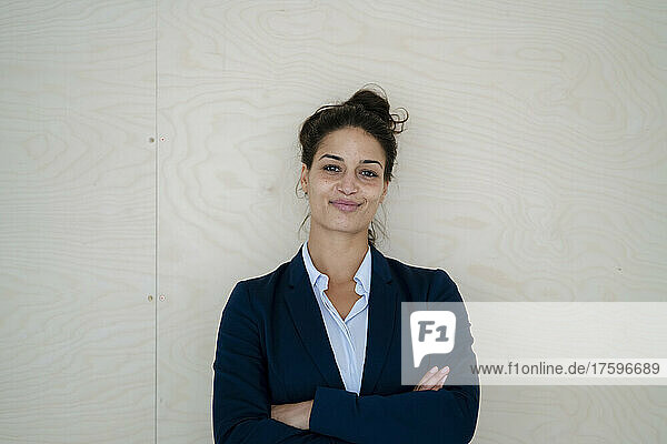 Businesswoman with arms crossed smiling in front of wall