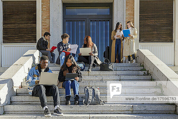 Friends studying over tablet PC and laptop on steps on campus