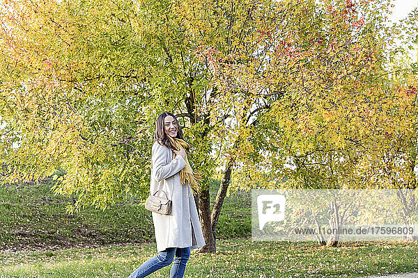Happy young woman walking by autumn trees in park