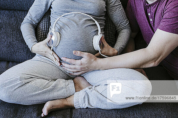 Pregnant woman with headphones over belly sitting with man at home