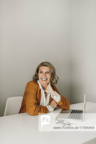 Happy senior freelancer sitting with laptop at desk