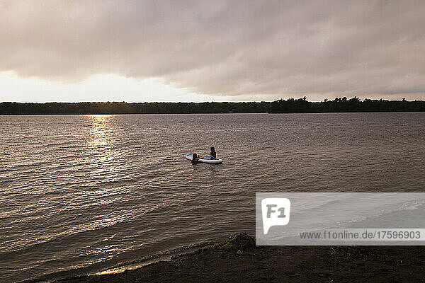 Mutter und Tochter sitzen auf dem Paddleboard und genießen den Sonnenuntergang
