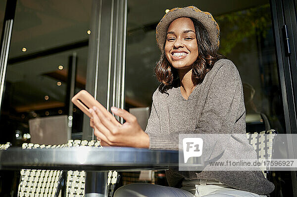 Happy woman with smart phone sitting at cafe on sunny day