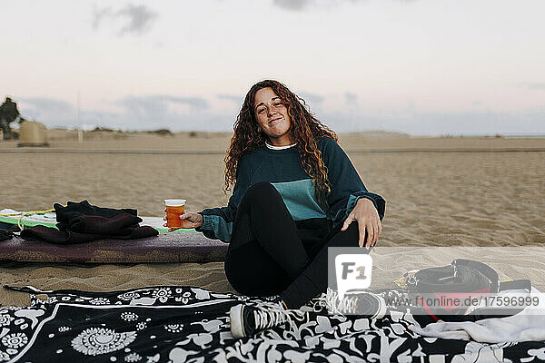 Young woman with beer cup sitting on sand at beach