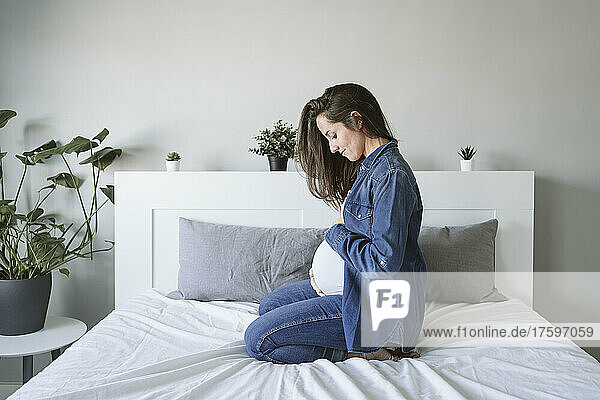 Pregnant woman with long hair sitting on bed at home