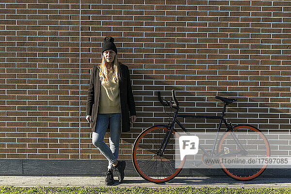 Young woman with bicycle in front of brick wall