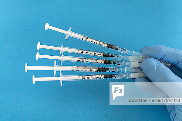 Doctor hand holding vaccine syringes against blue background