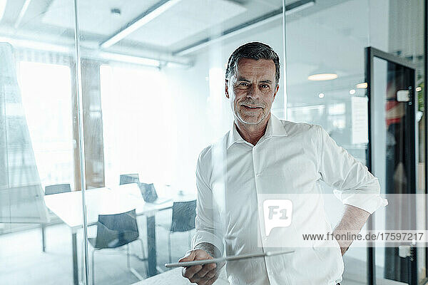 Working man with tablet PC leaning on glass wall at office