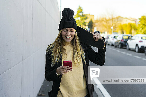 Smiling woman text messaging on smart phone on street