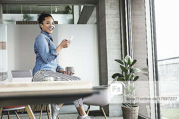 Smiling businesswoman sitting on desk at work place